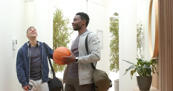 Arriving at hall, diverse male friends spinning basketball while opening door letting light inside - Powered by Adobe