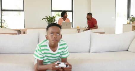 African American family closing laptop and joining child playing with white controller on couch