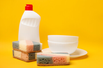 Kitchen sponges, dish soap and dishware on yellow background. Space for text