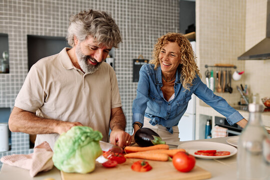 Portrait of happy senior mid aged mature couple prepering meal with fresh vegatebles in kitchen at hpme