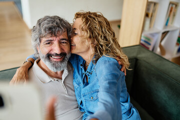 Portrait of a happy senior couple taking a selfie embracing hugging and having fun at home
