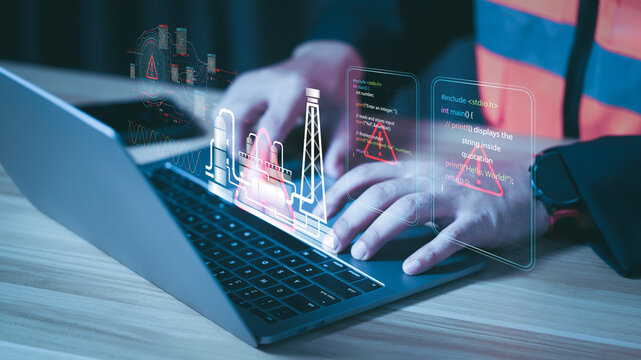 Engineer typing on laptop with system error hologram. Industrial cybersecurity warning and smart factory failure concept with red alert triangle and digital coding interface. - Powered by Adobe