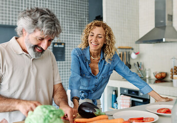 Portrait of happy senior mid aged mature couple prepering meal with fresh vegatebles in kitchen at...