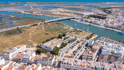 Fototapeta premium Tavira in Algarve shows the Gilao river, boats, and buildings from a high view. The area includes fields and water canals under a clear sky