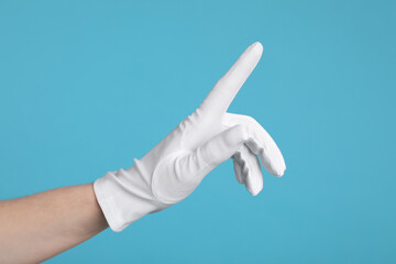 Woman in cloth glove pointing at something on light blue background, closeup