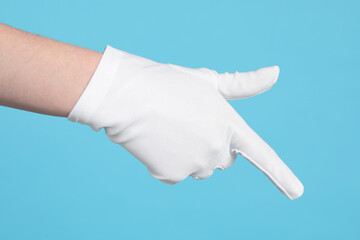 Woman in cloth glove pointing at something on light blue background, closeup