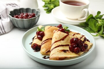 Delicious crepes with cherry jam and chocolate served on white table, closeup