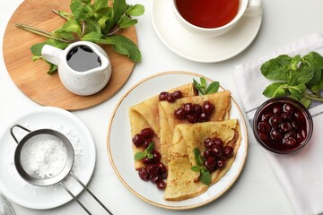 Delicious crepes with cherry jam served on white table, flat lay