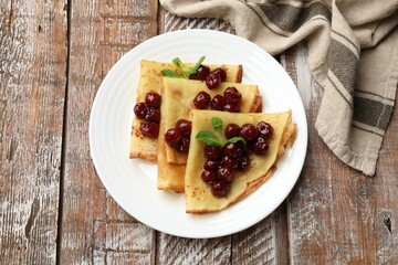 Tasty crepes with cherries and mint on wooden table, top view