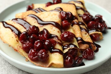Tasty crepes with cherries and chocolate on light table, closeup