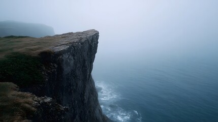 A rugged cliff edge shrouded in mist overlooking a vast blue ocean