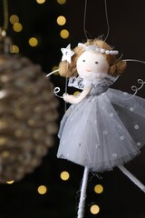 Naklejka premium Beautiful Christmas bauble and fairy doll hanging against black background with blurred lights, closeup