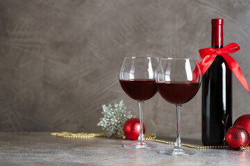 Glasses of red wine, bottle and Christmas decor on gray table. Space for text