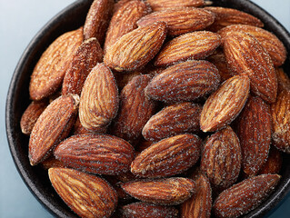 Fototapeta premium a bowl filled with whole almonds that have been coated in a light dusting of sugar, giving them a sparkling appearance. The almonds are arranged in a loose, natural cluster within the bowl