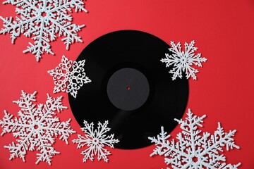 Vinyl record and decorative snowflakes on red background, flat lay. Christmas atmosphere
