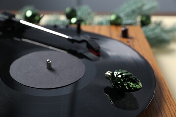 Wooden turntable with vinyl record and bauble on beige table, closeup. Merry Christmas and Happy...