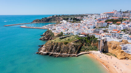 People relax on the beach and explore the marina in Albufeira, Portugal, as boats move in the water under a clear sky in summer time