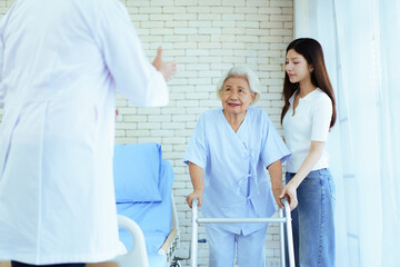 An elderly patient walks with a walker under caregiver and doctor supervision.