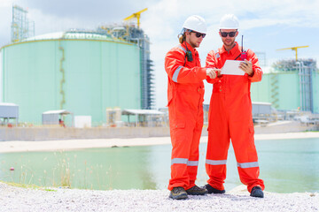 Engineers in protective gear review data on a tablet at an industrial site.