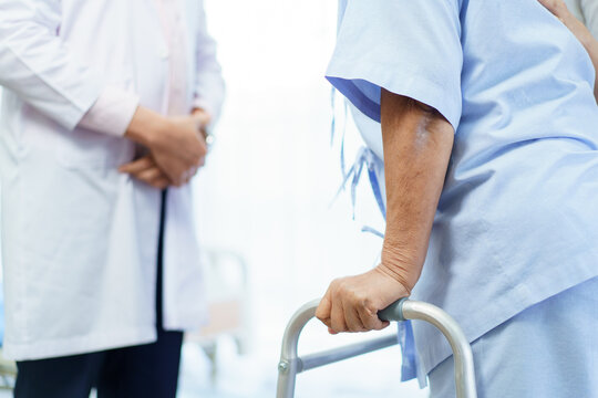 An elderly patient practices walking with a walker under medical supervision. - Powered by Adobe