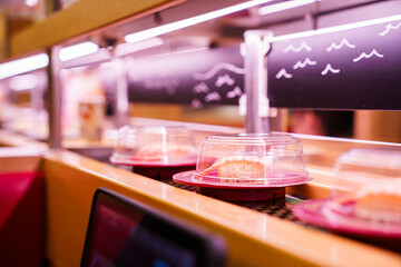 Sushi plates travel along conveyor belt in Japanese Kaiten sushi restaurant.