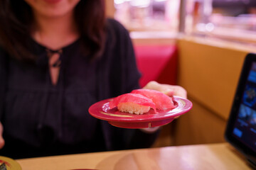 Woman holds plate of tuna sushi in Japanese conveyor belt restaurant.