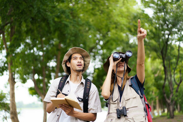 Two explorers use a notebook and binoculars while navigating through the forest.