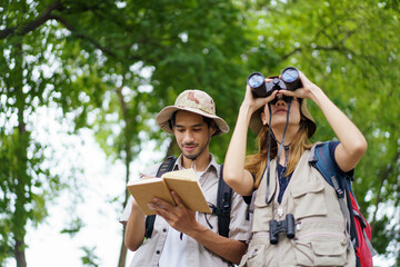 Two explorers use a notebook and binoculars while navigating through the forest.
