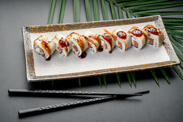 Glazed Eel and Salmon Roll with Sweet Sauce. A series of creamy maki rolls, topped with glazed eel and a sweet sauce, are presented on a decorative rectangular plate. © Анна Терелюк