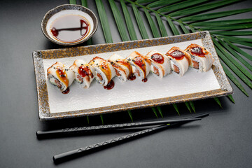 Glazed Eel and Salmon Roll with Sweet Sauce. A row of eight white maki rolls is topped with tender glazed eel, contrasting beautifully with the rich dark sauce. © Анна Терелюк