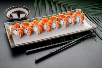 Sushi rolls with salmon and roe arranged on a plate. Soy sauce in a small bowl sits next to the plate. Two chopsticks are placed beside the dish