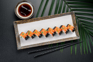 Naklejka premium Sushi rolls are lined up neatly on a plate. A small bowl with sauce sits nearby. Two chopsticks are placed next to the plate. A leaf adds detail to the scene
