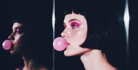 Ritratto primo piano volto di elegante e affascinante ragazza che fa una bolla con una gomma da masticare, sullo sfondo l'immagine riflessa in uno specchio