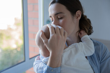 Mother holding and embracing infant baby with closed eyes showing care