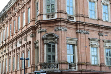 Historic city building with ornate classical architecture, pinkish stone facade, tall rectangular windows, and decorative balconies on a street corner.