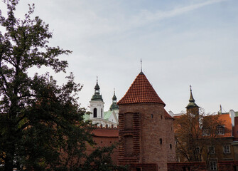 Fototapeta premium Classic view of the fortified Barbican red brick turrets and surrounding trees in the historic center of Warsaw, Poland.