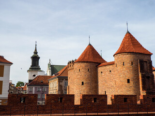 Obraz premium Wide shot of the impressive red brick Barbican fortification with its prominent circular towers against a clear blue sky in Warsaw Old Town.
