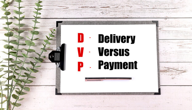Acronym DVP delivery versus payment written on clipboard with pen and green leaves on wooden background