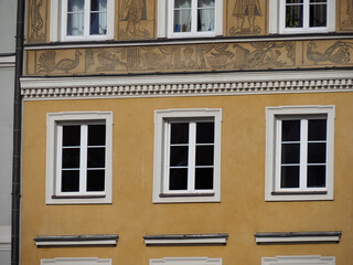 Obraz premium Symmetrical facade of a yellow historic building featuring four rectangular windows with white frames in Warsaw Old Town.