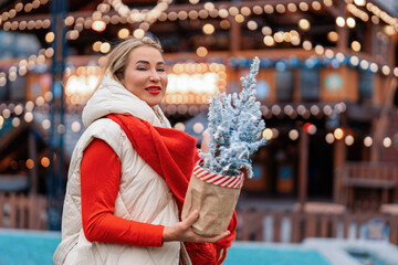 Woman holding small Christmas tree at festive outdoor market in winter evening