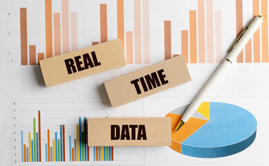 Text real time data on wooden blocks with financial graphs, charts and pen