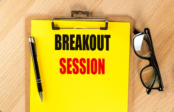 Text breakout session written on yellow clipboard with pen and glasses on wooden table