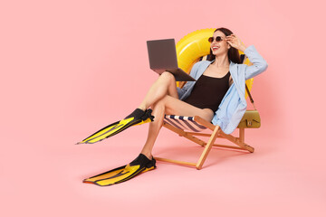 Businesswoman with laptop and flippers in deck chair on pink background © New Africa