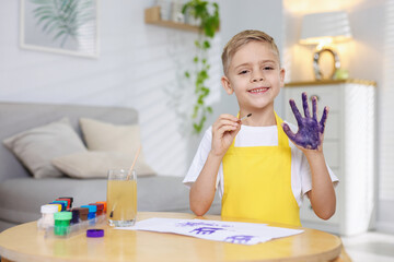 Cute little boy painting his handprint at wooden table indoors. Space for text