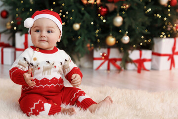 Cute baby in Santa hat on fluffy rug in room decorated for Christmas. Space for text