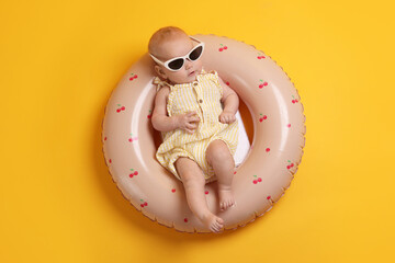 Cute little baby with sunglasses on inflatable ring against orange background, top view