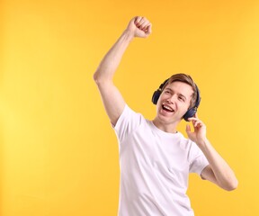Fototapeta premium Man with headphones listening to music and dancing on yellow background