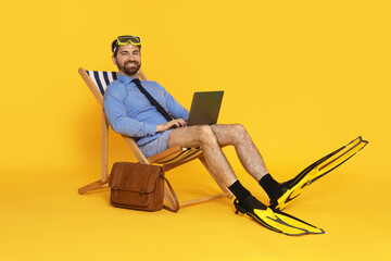 Businessman with diving mask, laptop and flippers in deck chair on orange background © New Africa