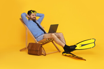 Businessman with diving mask, laptop and flippers in deck chair on orange background © New Africa