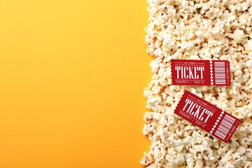 Tasty popcorn in paper cup and movie tickets on orange background, flat lay. Space for text